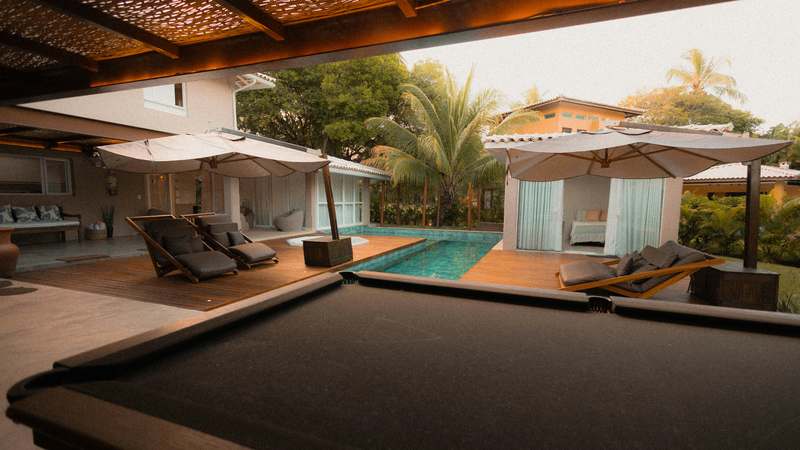 Modern poolside furniture setup with teak loungers, umbrellas, and blue pool backdrop