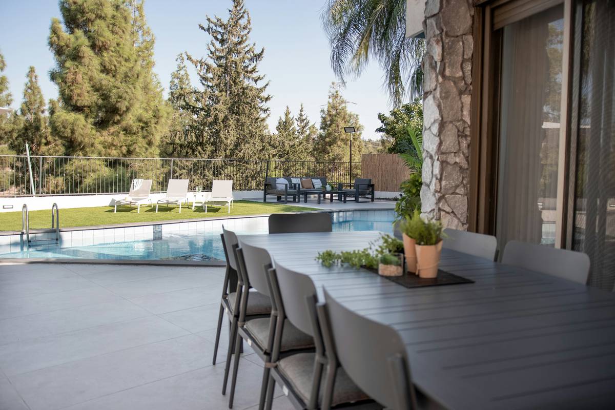 Stylish outdoor poolside furniture rental setup with teak table, cushioned lounge chairs, and umbrella by a residential pool